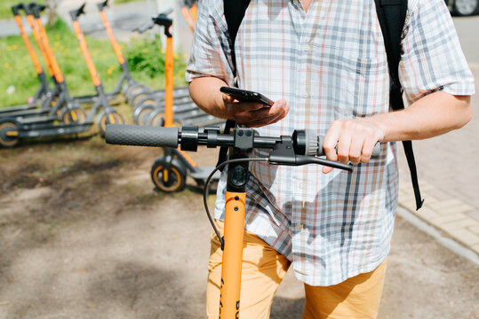 Close-up of man using smartphone mobile application to pay for rent of an electric scooter outdoors in park