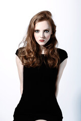 Fototapeta premium Beauty and fashion concept. Beautiful woman with long brown hair studio portrait in white background. Model sitting on chair with hands placed behind her back. Wearing black sexy dress. Smokey makeup