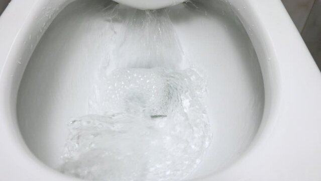 Close-up view of the white ceramic toilet in the modern bathroom. Open clean toilet in which water is washed into the sewer pipe. Process of flushing in a rimless toilet bowl