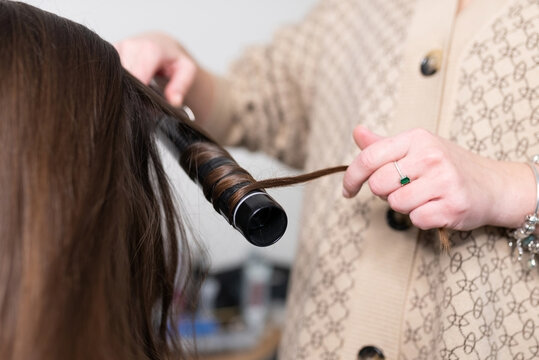The stylist curls the girl's hair with a curling iron