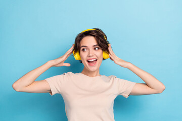 Photo of shiny excited woman wear beige t-shirt headphones enjoying music looking empty space isolated blue color background