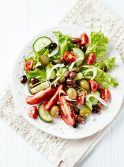 Healthy salad with various tomatoes, cucumber, olives and capers. White wooden background. Top view.