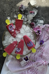 Berry ice cream in a plate with ice on a table with a kitchen towel. Homemade blackcurrant ice cream with viola flowers.