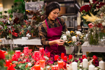 Asian woman in apron working in home goods store and setting out christmas decorations on showcase.