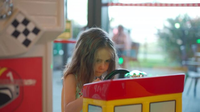 Little caucasian girl sitting on wheel toy electric car in amusement corner for children in shopping mall. Cute caucasian female child spending time while parents go shopping