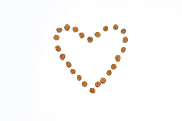 Dry pet food in the shape of a heart on a white isolated background. Healthy dry pet food in the center of the horizontal image. The concept of healthy food for animals