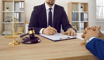 Male lawyer or judge in his office advises and develops contract for his client. Lawyer is sitting...