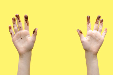 Children's hands smeared in chocolate on a yellow background. The concept of love for sweets and...