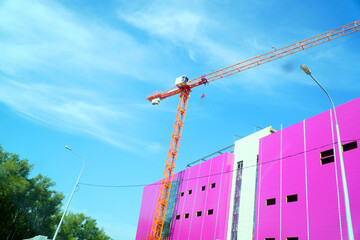 Construction crane near a pink building under construction against a blue sky