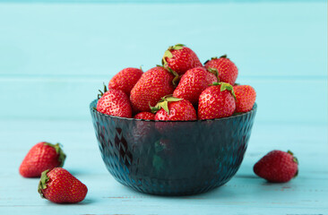 Ripe strawberries in bowl on blue background. Space for text