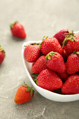 Ripe strawberries in white bowl on grey background