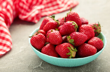 Ripe strawberries in blue bowl on grey background