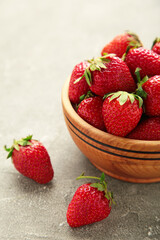Ripe strawberries in a wooden bowl on grey background
