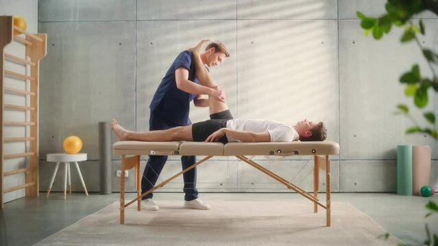 Advanced Sport Physiotherapy Specialist Stretching and Working on Specific Muscle Groups or Joints with Young Male Athlete. Sportsman Recovering from Mild Injury, Undergoing Rehabilitation.