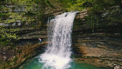 walk to Okatse Canyon - one person walking on the large stones covered with green moss under the small waterfall. High quality photo