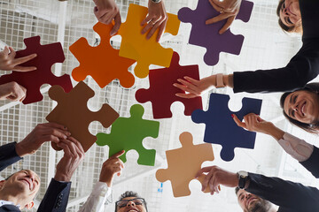 Business solutions. Joyful male and female office workers put together colored pieces of puzzle at...