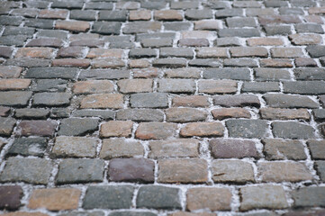 The road is paved with old cobblestones. Paving stones with snow. Winter architecture.
