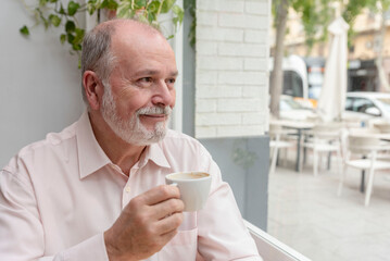 portrait of a smiling elder man looking out of the window enjoying a cup of coffee