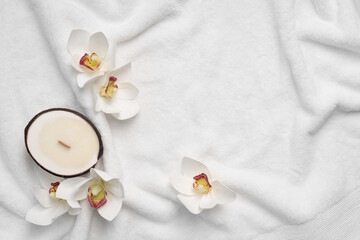 Aroma candle in coconut shell and orchid flowers on a white terry towel. Spa mockup with copy space.
