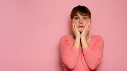 Portrait of a surprised attractive Caucasian girl isolated on a pink background, holding her head...