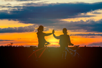 Fototapeta na wymiar Silhouette of happy mother and little daughter biking at sunset