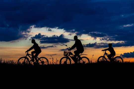 biker family. silhouette father with two kids on bikes at sunset
