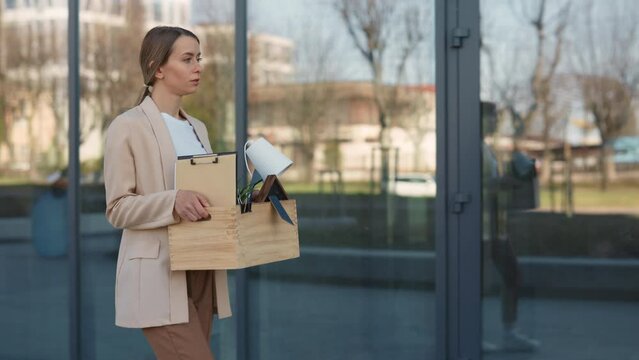 Desperate female manager carrying box with office stuff while living business centre. Caucasian young woman feeling depressed and frustrated for getting fired.