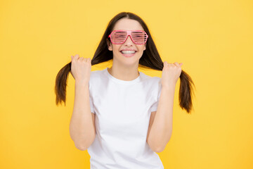 Beauty funny teenage girl with party glasses, yellow background. Surprised young woman with fun...
