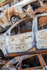 Fototapeta premium A view of burnt-out cars after rocket attacks by the Russian military. War of Russia against Ukraine. Civil vehicle after the fire. Cemetery of cars in the city of Irpin. Rusty pile of metal.
