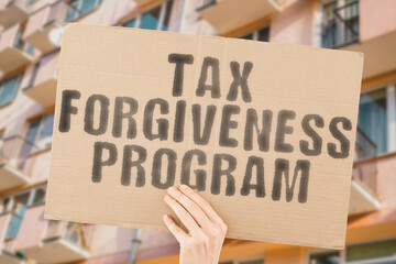 The phrase " Tax forgiveness program " is on a banner in men's hands with blurred background. Growth. Policy. Problems. Profit. Forgive. Reduce. Relief. Benefit. National. Free. Ignore. Issue. Law