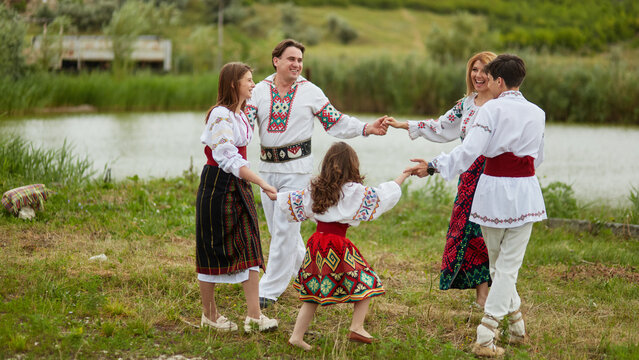 Full length image of a family with kids in traditional romanian dress in a countryside, park. Dancing outside together.