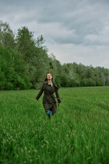 a beautiful woman in a long raincoat runs across a field in high grass in spring in cloudy weather