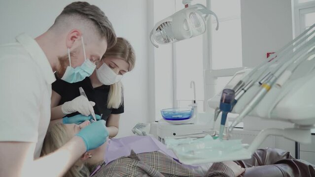 Two dentists, a man and a woman in protective masks and medical gloves, serve the patient at the dental clinic. The work of a dentist. Healthcare and medicine concept