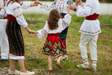 Frame image of a family with kids in traditional romanian clothes, dancing outside.