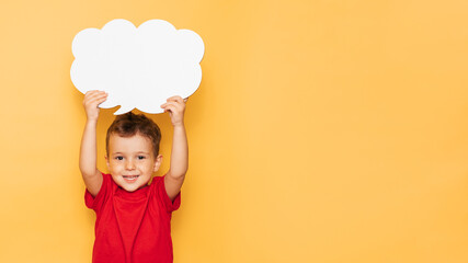 Studio portrait of a happy boy with a clean white board in the shape of a cloud on a bright yellow background, with a place for your text or advertising