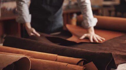 Deurstickers Man shoemaker hold different rolls natural leather brown, working with textile in workshop © Parilov