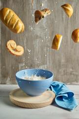 blue bowl with with splashes of milk flying chocolate muffins, palm tree,and milk bun on a rustic grey background. food art