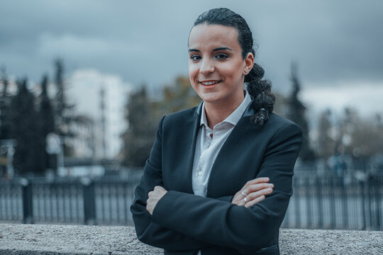 Secretaria de cabello oscuro formal con seriedad y de pie de brazos cruzados reflexionando con una sonrisa en el centro de la ciudad parada por la calle para llegar a su
