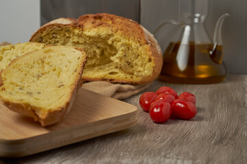 freshly baked bread on a wooden cutting board with oil and tomatoes on a grey background