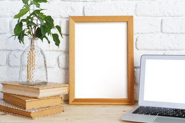 Blank picture frame on wooden table with books and laptop