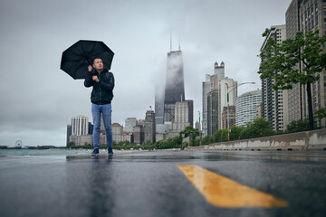 Rainy and windy day in city. Man with umbrella walking against Chicago cityscape..