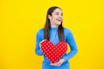 Girl feeling love. Portrait of lovely sweet cute pretty girl hold red paper card heart isolated over yellow background. Beautiful girl holding heart, love shape.