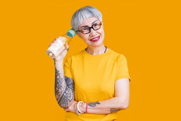 healthy lifestyle old senior asian female tattoo wear casual yellow colour cloth hand hold pure water bottle look at camera freshness smiling studio shot on yellow colour background