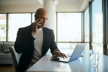 African American businessman talks on cell phone while working on laptop in the office.