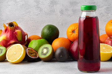Various fruits and freshly squeezed fruits juice in bottle on gray background