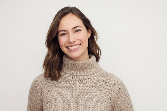 Portrait of a smiling brunette woman in a warm beige sweater, looking happy in camera.