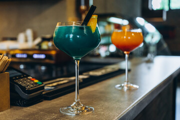 two glasses with colored cocktails on the bar counter