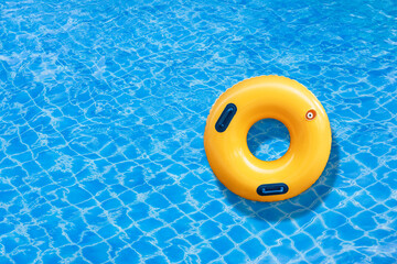 Yellow ring floating in a blue wave water on the outdoor swimming pool. Summer holidays