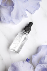 Serum with floral extracts for skincare. Nature cosmetics in glass bottle with pipette and iris flowers on marble background. Face and body care spa concept.