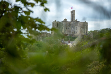 View of medieval Warkworth Castle from afar with tree and foliage in the way for artistic effect